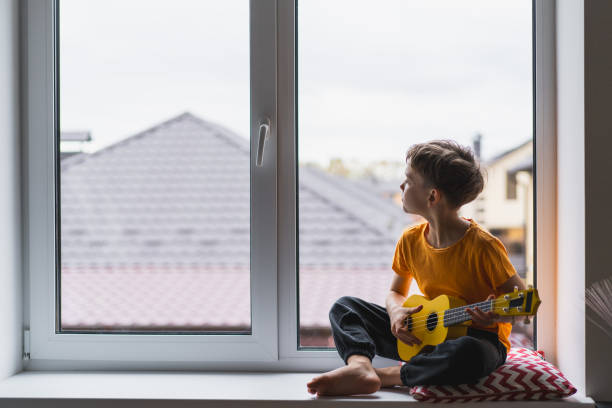 istock Boy playing a yellow ukulele while in his room at home 2191281818