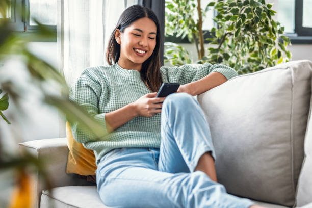 istock Smiling young woman using her mobile phone while sitting on sofa at home 2191287042