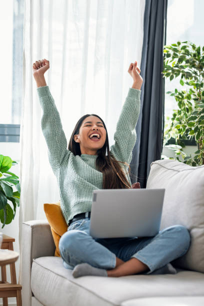 istock Pretty motivated woman celebrating something while working with laptop sitting on a couch at home 2191287078