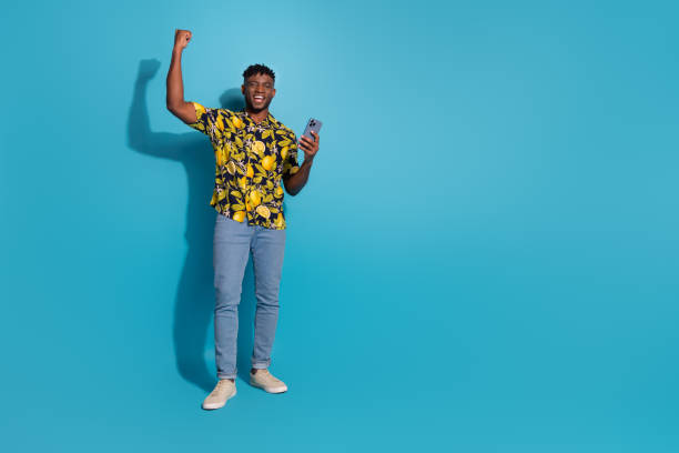 istock Joyful young man celebrating success on smartphone with a bright smile against blue background 2191291792