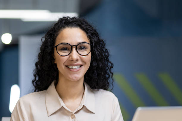 istock Smiling professional woman with glasses sitting in modern office environment, displaying positive attitude and confidence on the job, engaged in work tasks, fostering productivity and teamwork. 2191292002