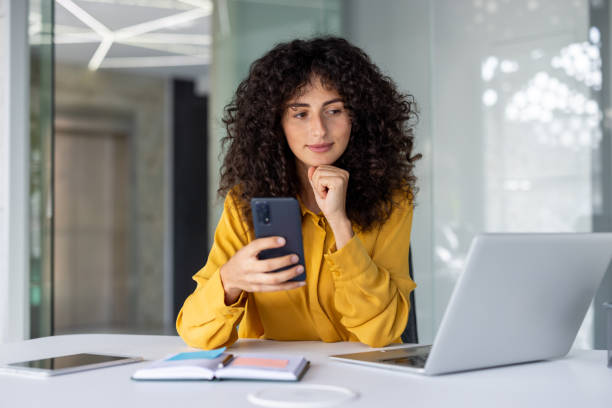 istock Woman working remotely with smartphone and laptop in modern office setting 2191294332