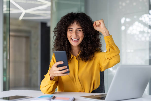 istock Ecstatic woman celebrating success on smartphone while working in modern office environment 2191297554
