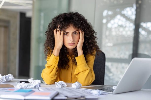 istock Stressed businesswoman sitting at desk surrounded by papers and laptop, experiencing work-related stress in modern office environment 2191297621
