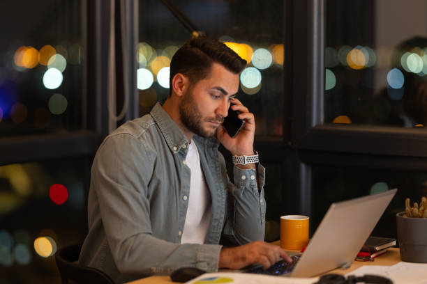 istock Focused businessman working late at night in office using laptop and talking on phone 2191300973