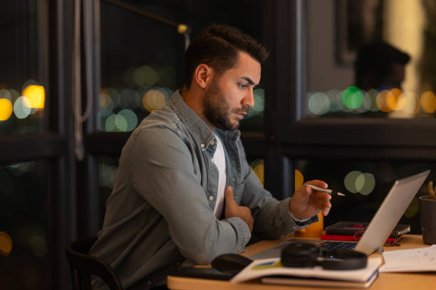 istock Focused young man working late on laptop in modern office with city view 2191300974