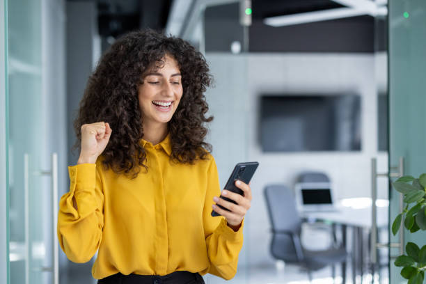 istock Excited woman celebrates success while looking at smartphone in modern office setting 2191303245