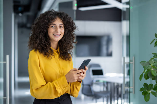 istock Smiling woman in office holding a smartphone during a break 2191303483