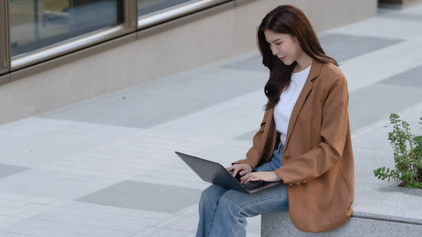 istock woman working on laptop outdoors, wearing brown blazer and jeans, focused on her task. modern setting features clean, minimalist design 2191306089