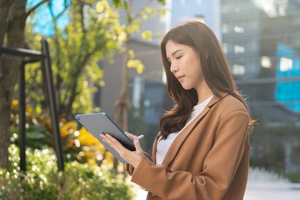 istock woman using tablet outdoors in modern urban setting, surrounded by greenery and buildings, showcasing blend of technology and nature 2191306125