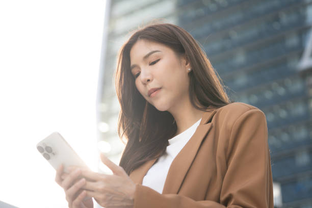 istock woman using smartphone outdoors, wearing brown blazer, with modern city backdrop. sunlight creates soft glow, enhancing urban atmosphere 2191306135