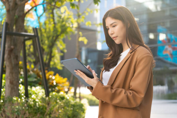 istock woman using tablet outdoors in modern urban setting, surrounded by greenery and colorful art. She appears focused and engaged with her device 2191306137