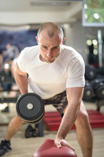 Focused individual exercises with a dumbbell, demonstrating strength training and fitness dedication inside a gym environment.