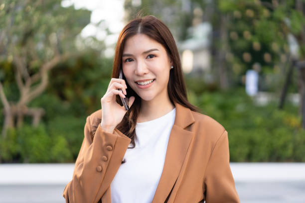 istock young woman smiles while talking on her phone outdoors, dressed in stylish brown blazer. lush greenery in background adds refreshing touch to scene 2191306347