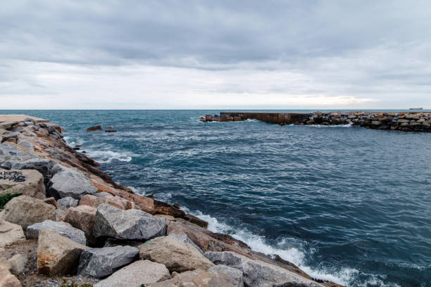 A rocky coastline with a breakwater extending into the sea under a cloudy sky.