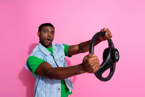 istock Energetic young man with a steering wheel against a vibrant pink background, expressing excitement and enthusiasm. 2191309437