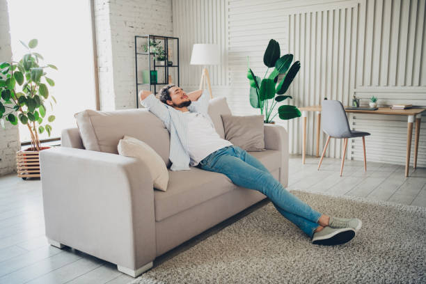 istock Young man relaxing on a comfortable sofa at home in a bright modern living room interior during a sunny day 2191311054