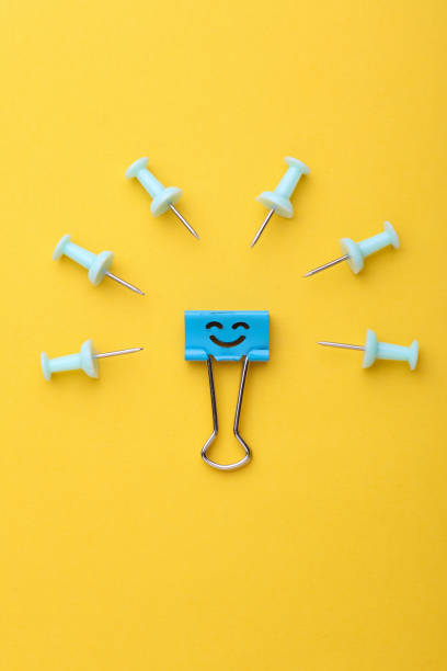 Binder clip with smiling face and paper pins on yellow background. Leadership, uniqueness, career growth. Business concept.