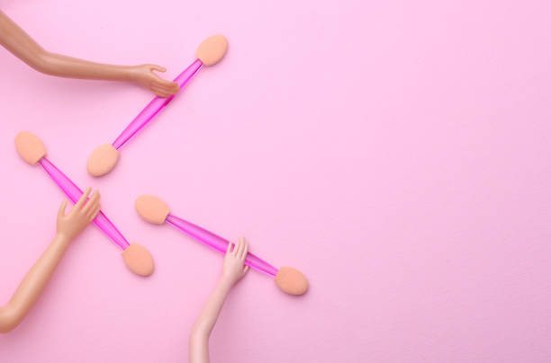 Doll's hands holding makeup sticks on pink background