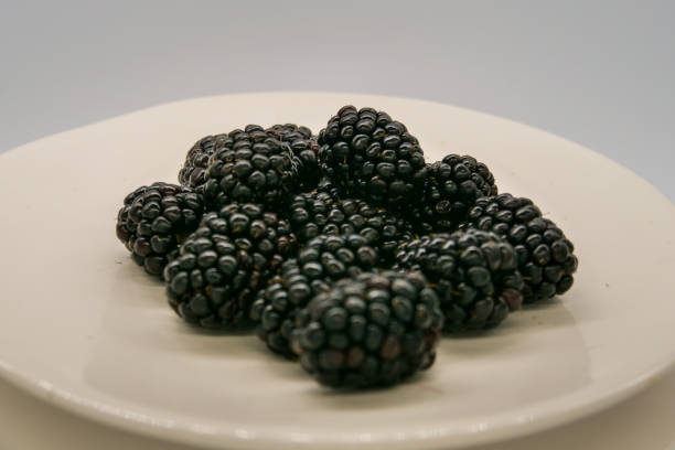 Fresh black mulberries on a white plate in front of a white background