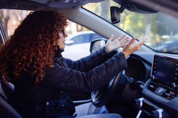 Stressed businesswoman arguing with raised hands while driving her car in traffic