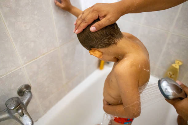 A loving mother gently shampoos her young son's hair as they sit by the bathtub, rinsing off sand and saltwater after a fun day at the beach.