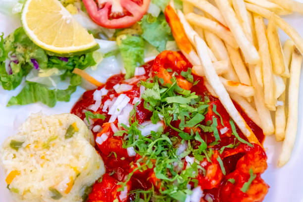 Close-up of a plate of loaded nachos served in a black ceramic dish. The dish is generously topped with fresh salsa, white cream, sliced avocado, and crisp tortilla chips. A juice accompanies the appetizer, set against a striking red wooden table background.
