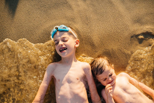 High angle view of two boys lying on a coast line and having fun in the sun on their summer vacation