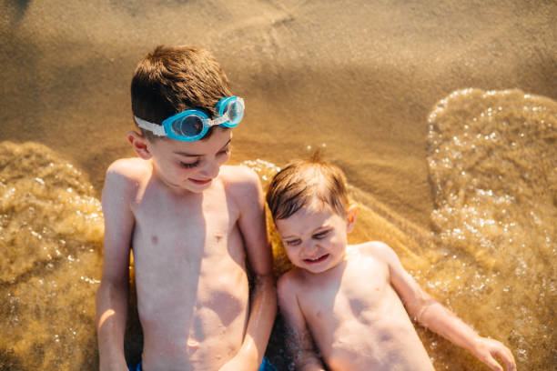 istock Two boys lying on a coast line and having fun in the sand 2191330930