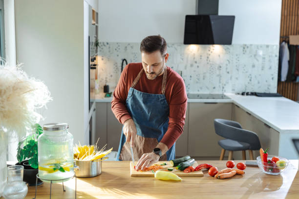 istock Man in apron preparing fresh vegetables in a well-lit modern kitchen 2191331059