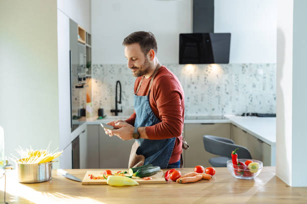 istock Man enjoying using smartphone while cooking healthy food in a modern kitchen 2191331069