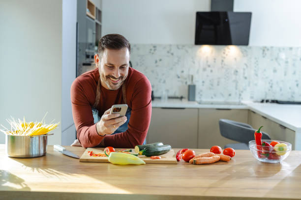 istock Man enjoying using smartphone while cooking healthy food in a modern kitchen 2191331072