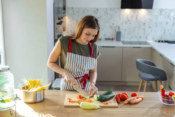 istock Young woman cutting vegetables in a modern kitchen with focused attention 2191331630