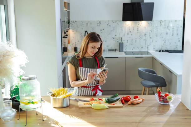 istock Woman using smartphone in modern kitchen while preparing fresh food 2191331657