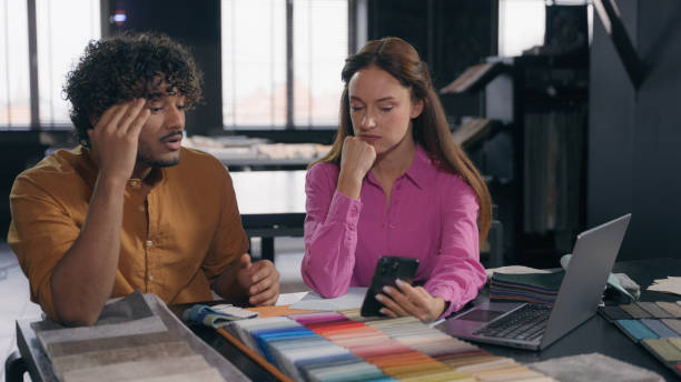 istock Two designers male female colleagues in modern design studio looking at fabric samples discussing color textile for interior angry Arabian Indian man talk with Caucasian woman problem misunderstanding 2191331721