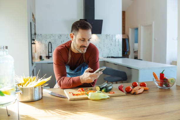 istock Handsome mid adult man using smartphone while cooking 2191331851