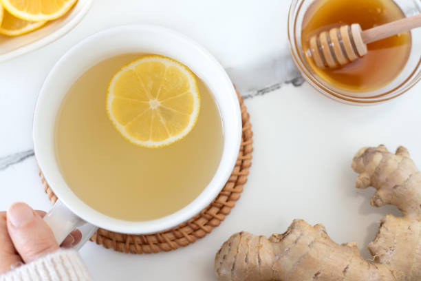 istock Hand holding cup of ginger lemon tea on white marble table with honey, top view 2191334971