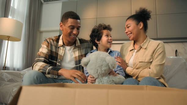 istock Happy little boy son kid open box unpacking parcel take teddy bear fluffy toy birthday present surprise excited joyful child smiling love parents African American family moving in new home relocation 2191343432