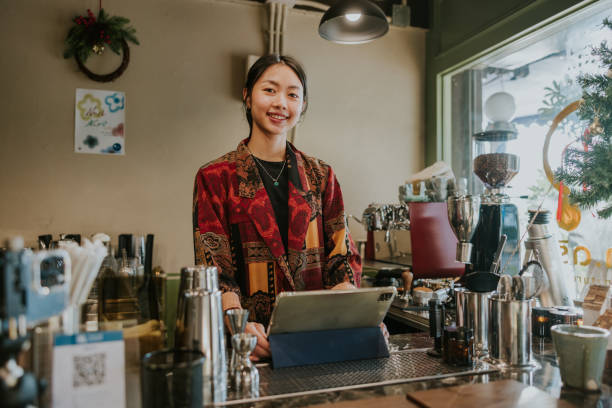 istock Real artist Barista looking at camera, in unique Christmas theme Attire Using a Digital Tablet in a Cozy Café During the Holiday Season
