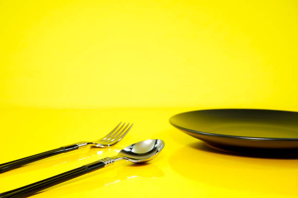 Cutlery set together with black ceramic plate close up view on yellow background food concept photography