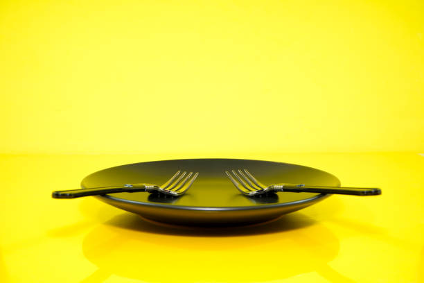 Cutlery set together with black ceramic plate close up view on yellow background food concept photography