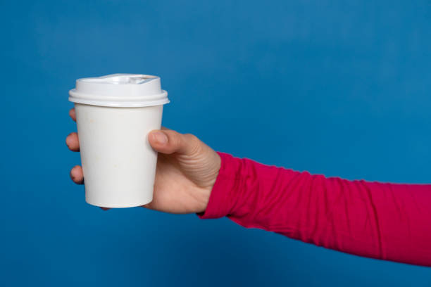 istock Woman holding white disposable coffee cup on blue background 2191368267