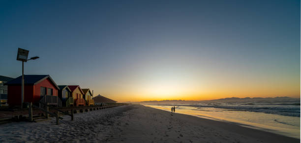 Cape Town, South Africa - August 31, 2022: people run on Muizenberg beach, next to the colorful beach huts, in Cape Town, South Africa