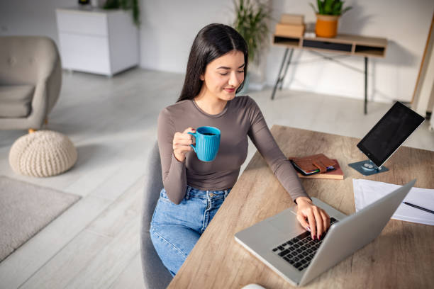 istock Woman drinking coffee and working on a laptop indoors 2191374200