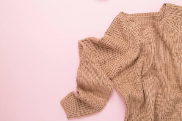 Beige knitted sweater on color background, top view