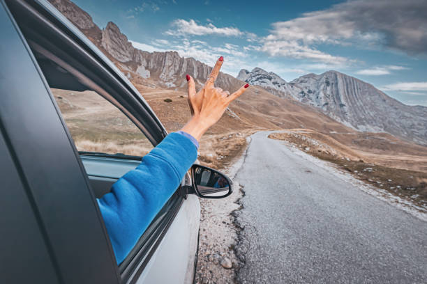 istock Woman making rock and roll hand gesture from car window while enjoying road trip in the mountains 2191380793