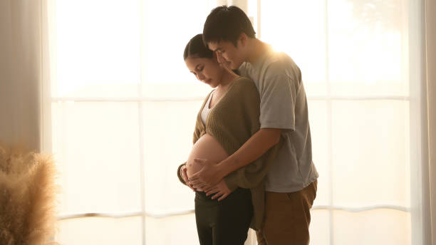 Couple Embracing During Pregnancy in Softly Lit Room Near Window