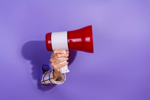 A hand holding a red megaphone breaking through a purple background, symbolizing communication and announcement