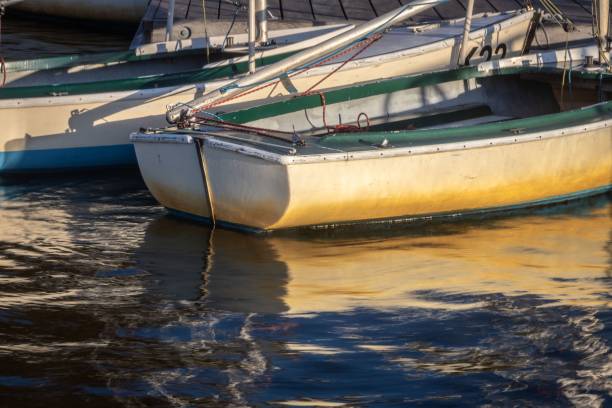 Sunlit boats docked at a marina with reflections on the water, capturing a serene nautical scene.