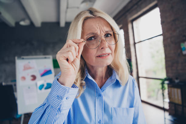 istock Mature businesswoman in a modern office environment with a thoughtful expression, wearing elegant striped shirt and glasses in daylight 2191390356